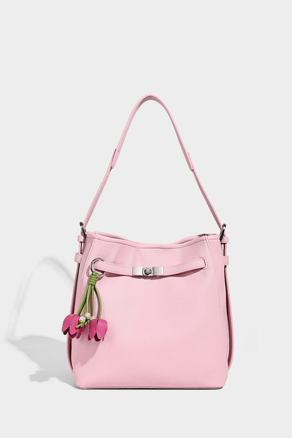 Soft-structured pebbled bucket shoulder bag with front turn-lock strap detail, adjustable strap, and hanging floral tassel