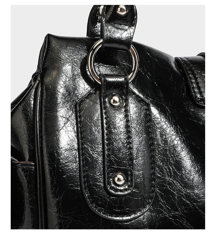 Glänzende, geknautschte Barrel-Satchel mit zwei oberen Tragegriffen, vorderem Klappen-Riemen-Panel, Ring- und Nietenbeschlägen sowie einem abnehmbaren