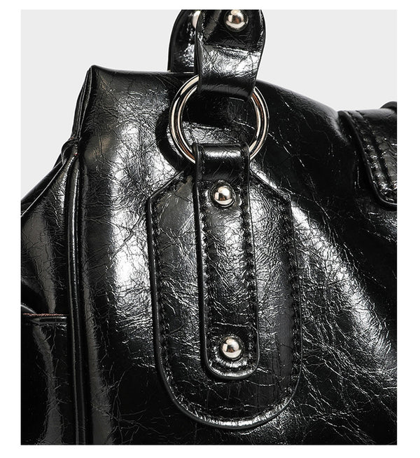 Glänzende, geknautschte Barrel-Satchel mit zwei oberen Tragegriffen, vorderem Klappen-Riemen-Panel, Ring- und Nietenbeschlägen sowie einem abnehmbaren