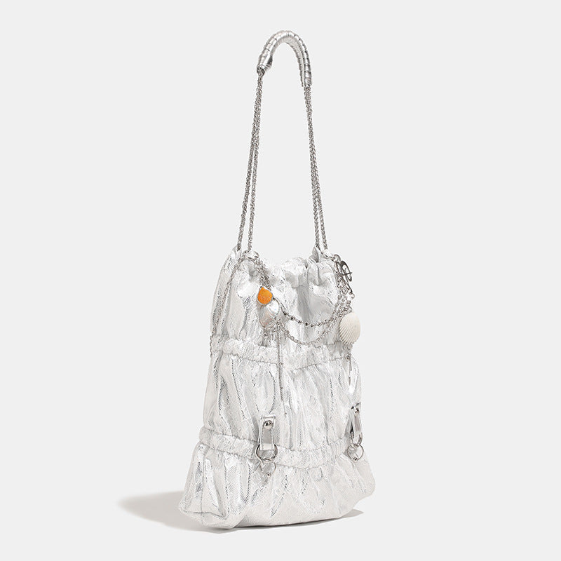 Slouchy lace-overlay bucket bag with silver chain strap, draped chain detail, shell charms, and drawstring top closure, front