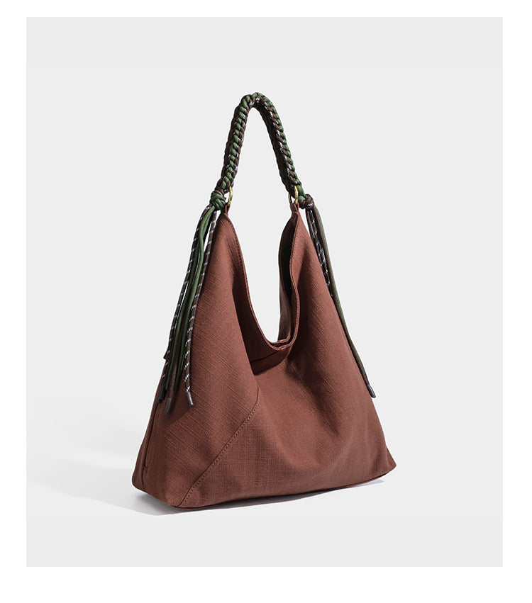 Soft slouchy cream canvas shoulder tote with braided brown and green cord handle, gold-tone ring hardware, and tassel trim