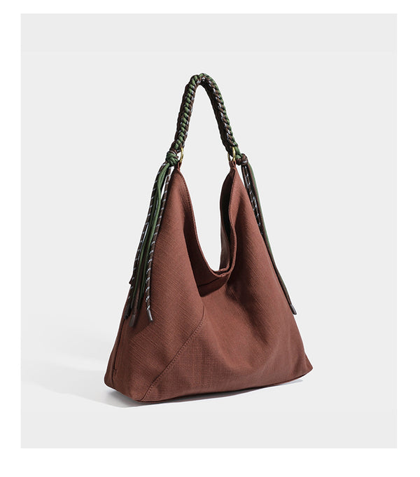 Soft slouchy cream canvas shoulder tote with braided brown and green cord handle, gold-tone ring hardware, and tassel trim