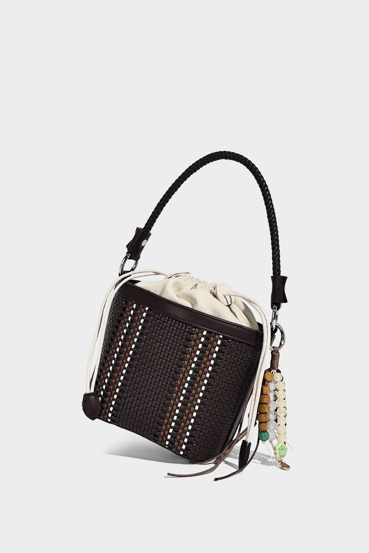 Small woven bucket bag with drawstring top, braided handle, detachable crossbody strap, and silver-tone ring hardware, detail