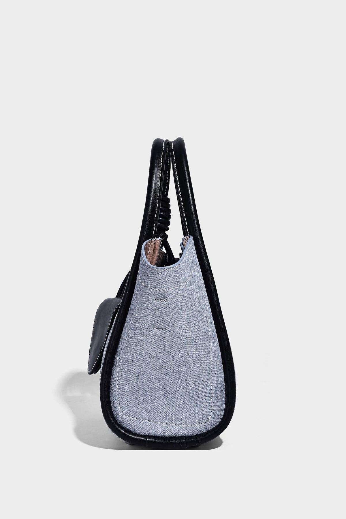 Light blue denim trapezoid tote bag with black leather-look trim, knotted top handles, detachable crossbody strap, front