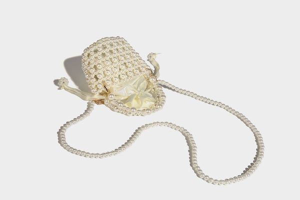 Elfenbeinfarbene Mini-Beuteltasche aus Kunstperlen mit Satinzugband-Innenfach, Ringbeschlägen in Goldoptik und gewölbtem Perlenhenkel