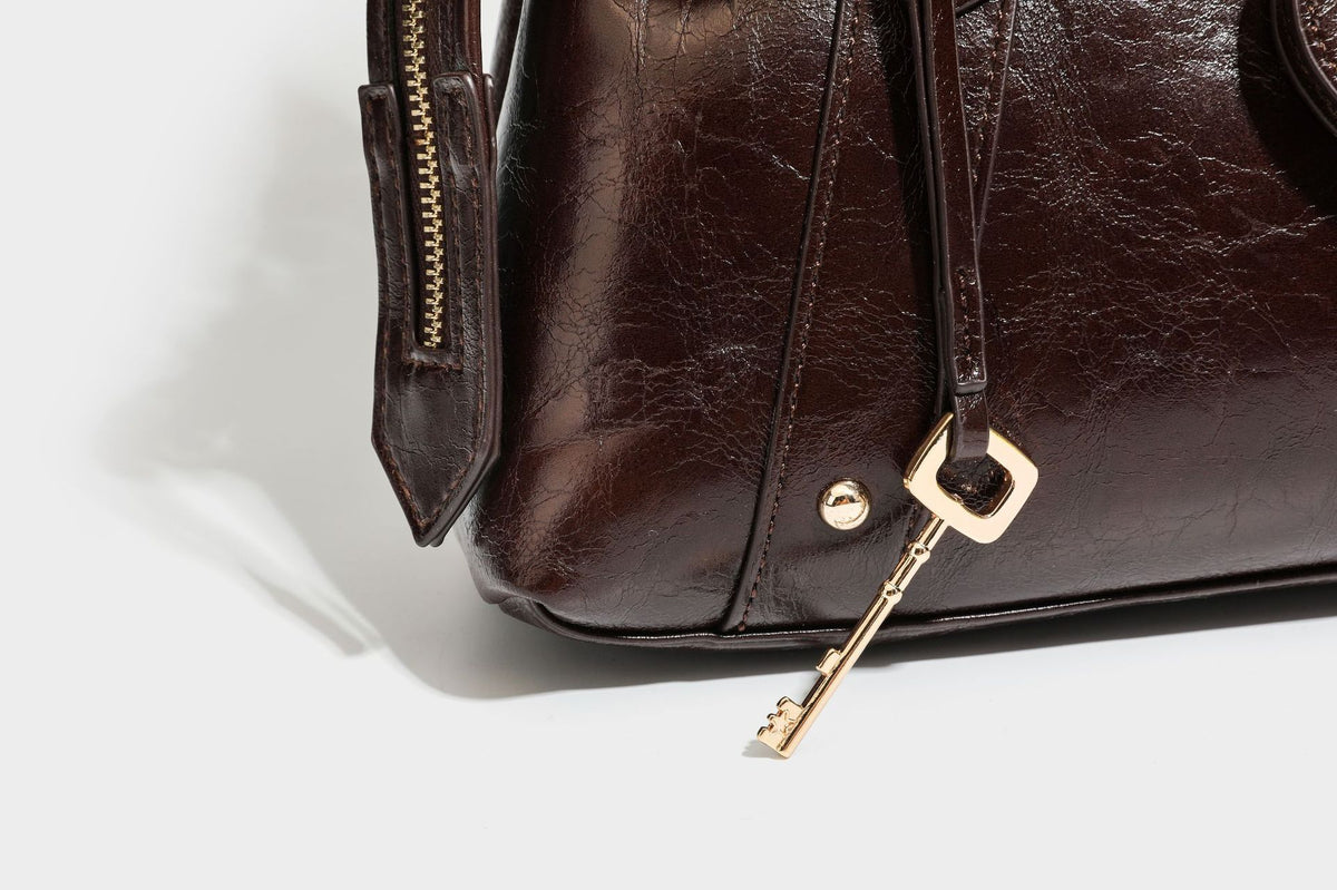 Structured leather-look satchel bag with heart padlock charm, star charm, gold-tone buckle hardware, dual top handles, and