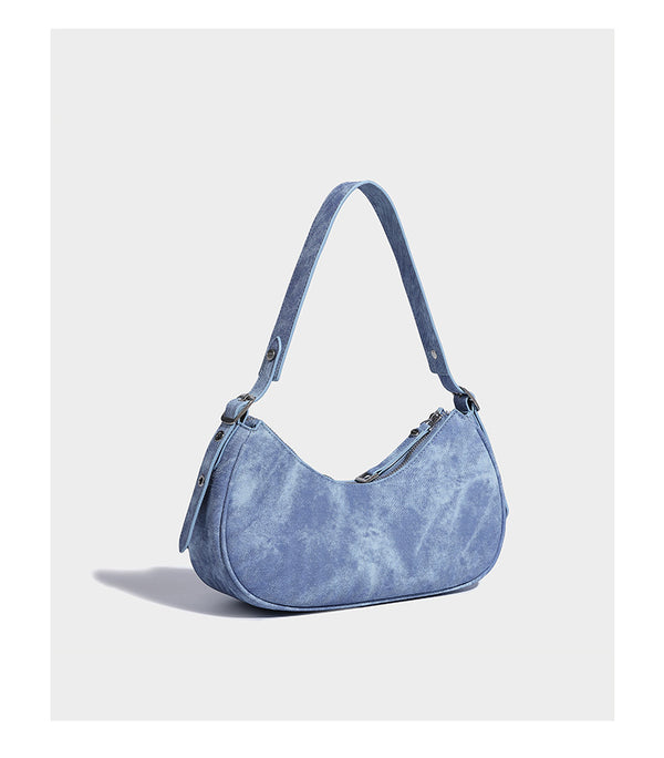 Crescent shoulder bag in washed blue denim-look PU with stacked buckle straps, front zip pocket, and silver-tone hardware
