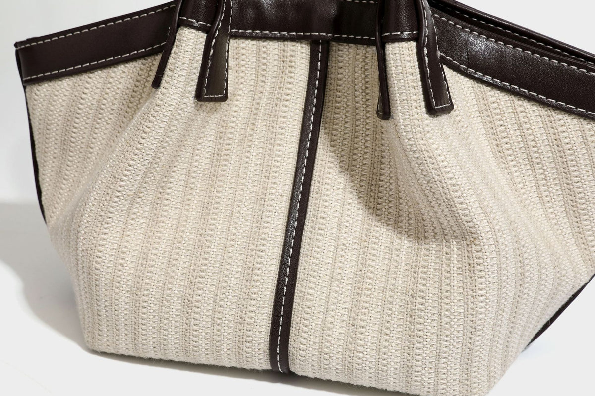 Cremefarbene geflochtene Tote-Bag mit dunkelbraunen Besätzen in Lederoptik, kontrastierenden weißen Nähten, zwei oberen Henkeln und abnehmbarem Schulter