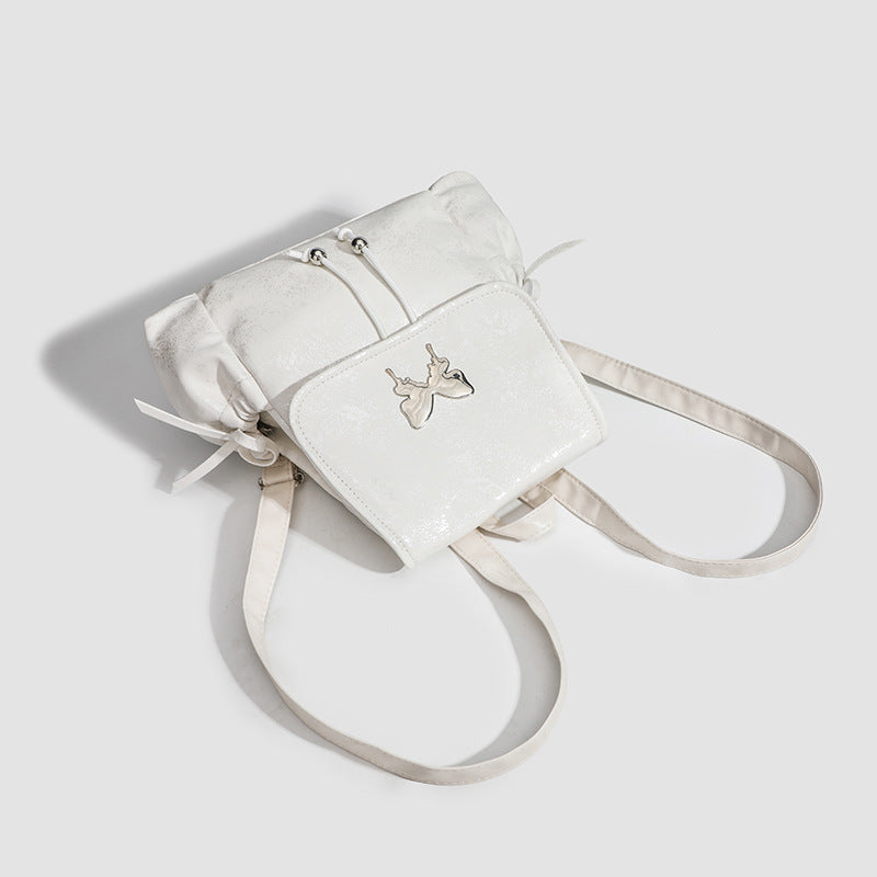 Compact white pearlescent flap backpack with silver-tone bow hardware and drawstring closure, detail view 3