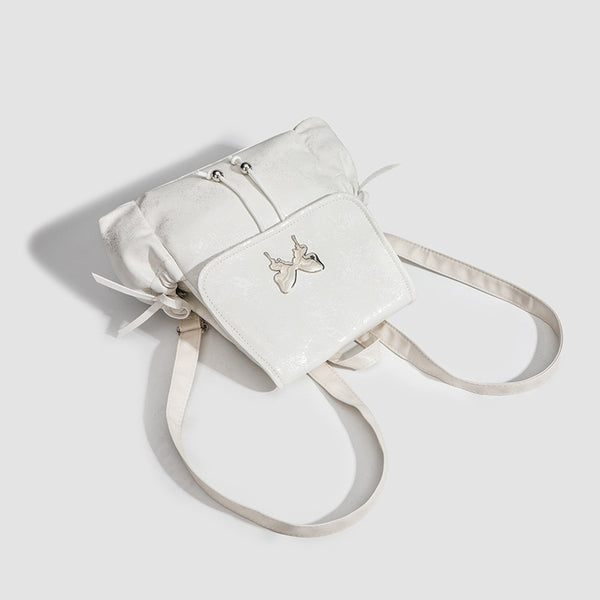Compact white pearlescent flap backpack with silver-tone bow hardware and drawstring closure, detail view 3