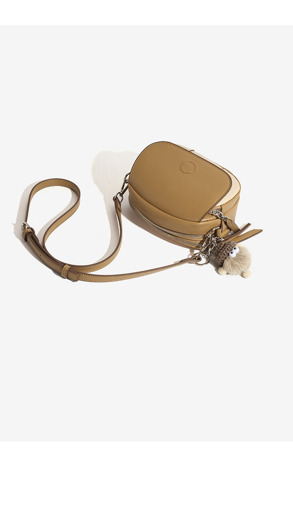 Kompakte zweifarbige ovale Umhängetasche in Lederoptik in Tan und Creme mit silberfarbenen Beschlägen und flauschigem Anhänger, Detailansicht 12
