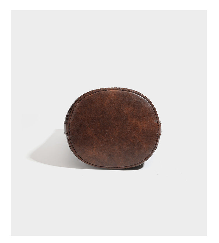 Structured woven-texture leather-look bucket bag in brown with knotted top handles, small front flap pouch, and adjustable