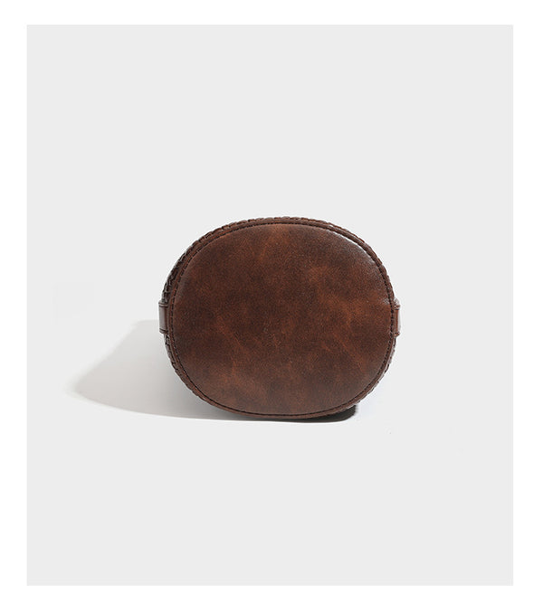 Structured woven-texture leather-look bucket bag in brown with knotted top handles, small front flap pouch, and adjustable