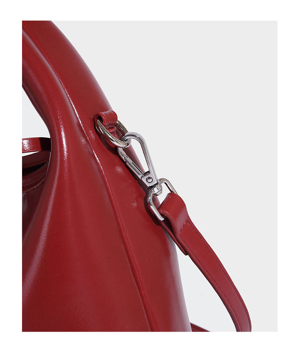 Kleine kuppelförmige Henkeltasche in glänzender Lederoptik mit Kordelzugverschluss, weißem Spitzen-Schleifenanhänger und silberfarbenen Metallbeschlägen