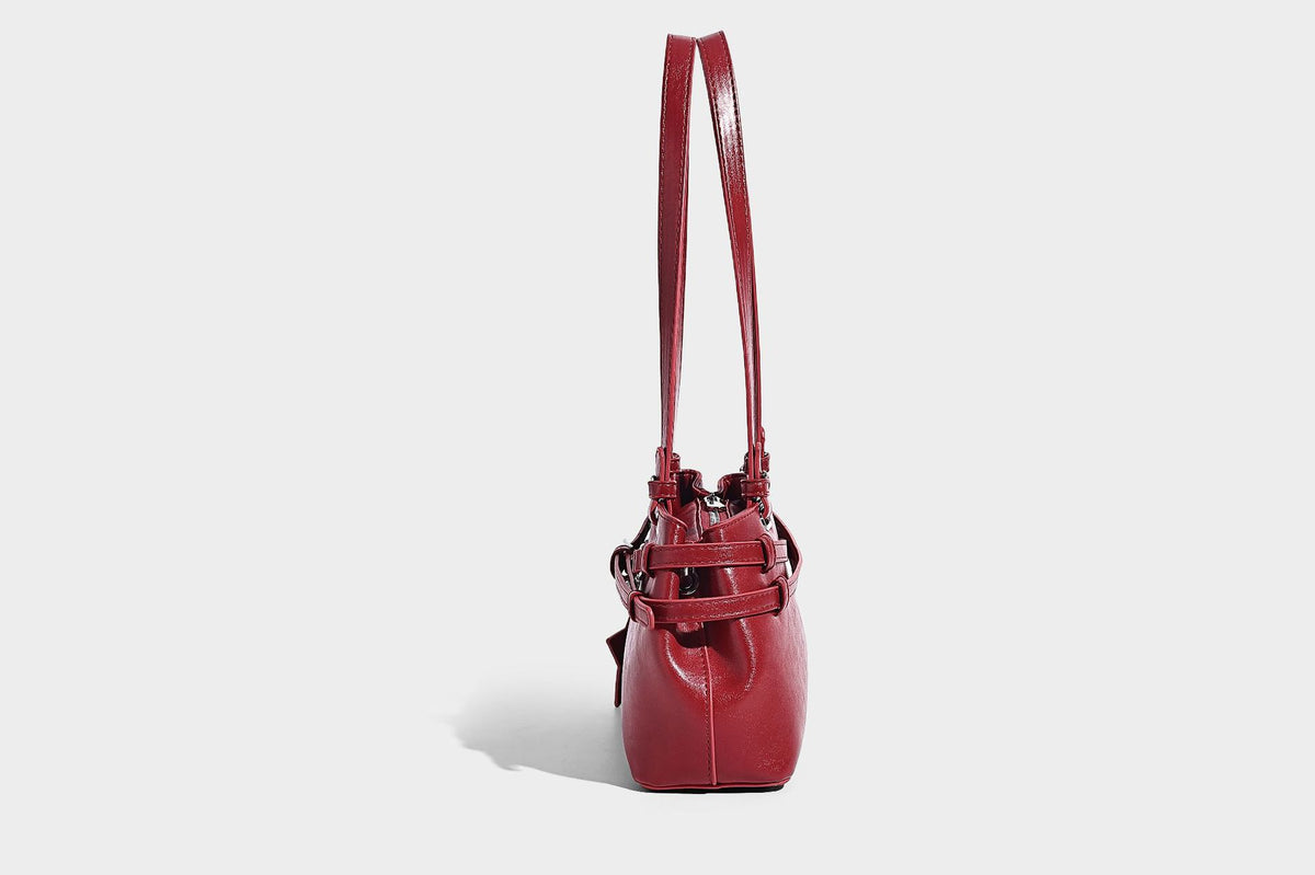 Structured glossy leather-look shoulder bag with wraparound belt straps, silver-tone hardware, and dangling star charm