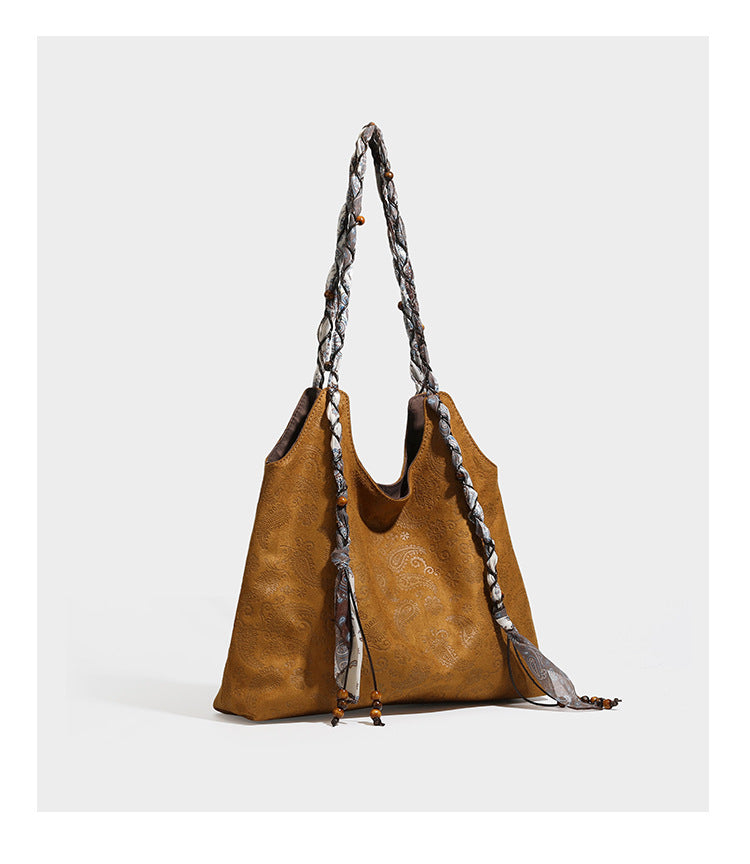 Slouchy paisley-embossed suede-look shoulder tote bag with braided patterned fabric straps and wood bead accents, detail view