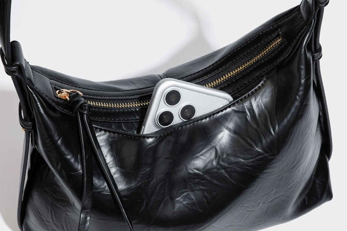 Übergroße, lässig fallende Hobo-Schultertasche aus glänzendem, geknittertem Material in Lederoptik mit Reißverschluss und Emblem-Beschlägen in Goldoptik, Detailansicht