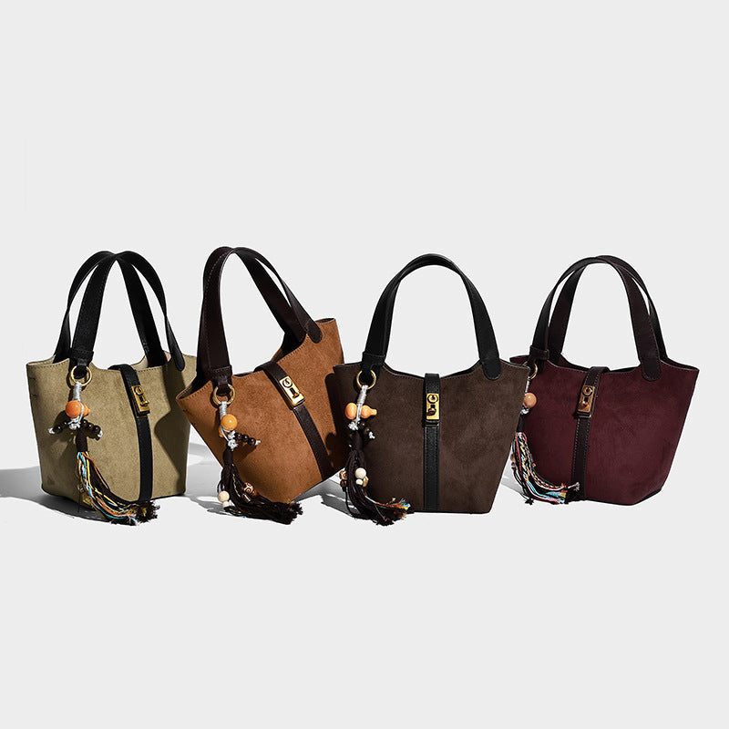 Small structured trapezoid tote bag in matte suede-look finish with black contrast trim, gold-tone front clasp, tassel charm