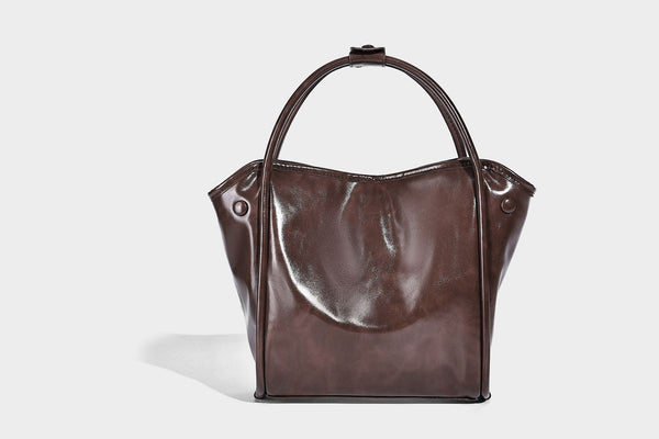 Glossy leather-look structured tote bag with rounded top handles, detachable shoulder strap, embossed front emblem, and side