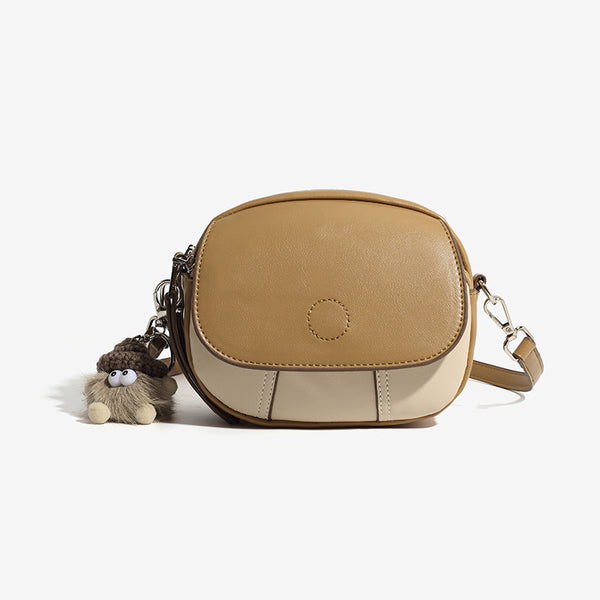 Kompakte zweifarbige ovale Crossbody-Tasche in Hellbraun und Creme mit Lederoptik, silberfarbenen Beschlägen und flauschigem Anhänger, Vorderansicht