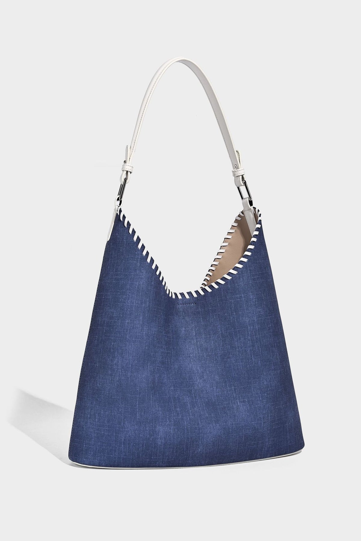Denim-blue hobo tote with white leather-look shoulder strap, contrast whipstitch trim along curved open top, and silver-tone