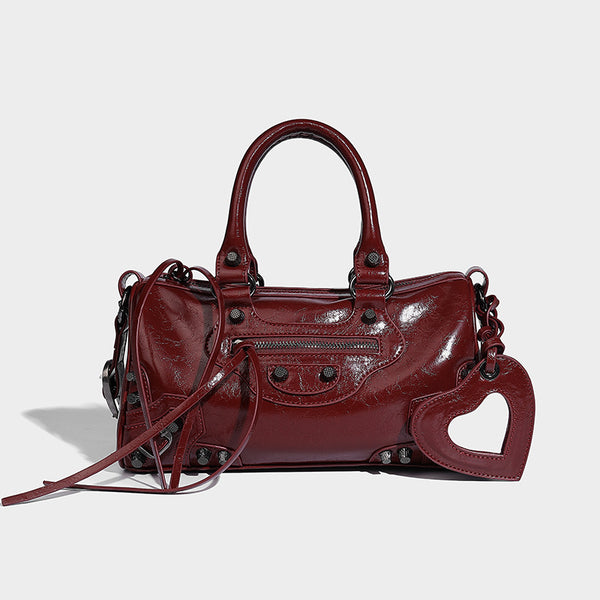 Glossy studded mini satchel bag with braided top handles, front zip pocket, heart charm, and detachable crossbody strap