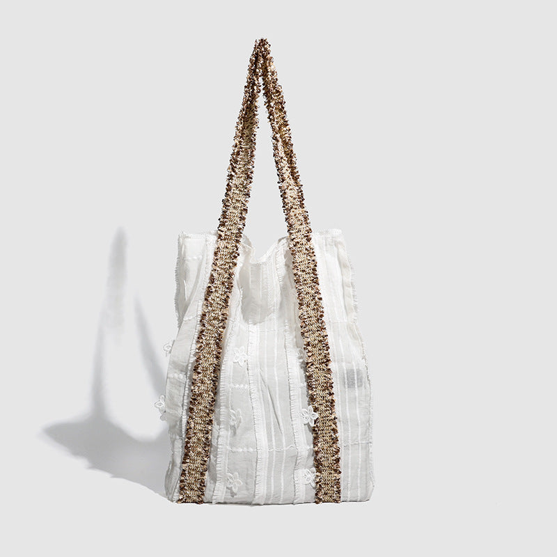 Offwhitefarbener weicher Canvas-Schultershopper mit offenen Seiten und braun-goldfarbenen Jacquard-Gurtbändern mit Blumenmuster, lässig rechteckige Form, Detailansicht