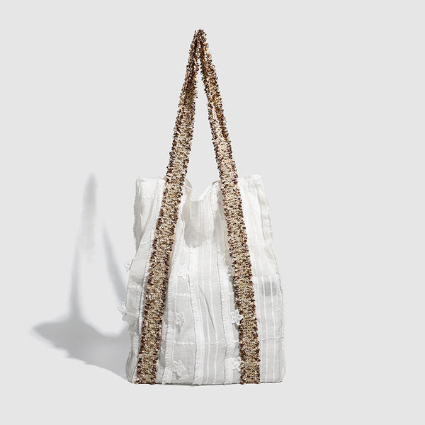Offwhitefarbener weicher Canvas-Schultershopper mit offenen Seiten und braun-goldfarbenen Jacquard-Gurtbändern mit Blumenmuster, lässig rechteckige Form, Detailansicht