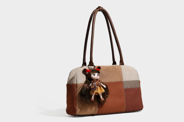 Boxy patchwork suede-look shoulder tote in tan, beige, rust, and brown panels with double brown straps and hanging doll