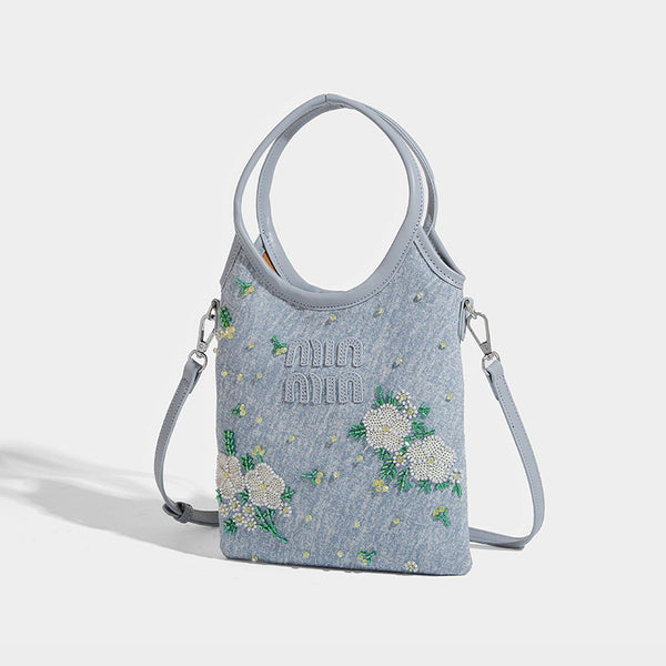 Kleine hellblaue Mini-Tote-Bag aus Stoff mit weißer Blumenverzierung aus Perlen, runden Tragegriffen, silberfarbenen Metallelementen und