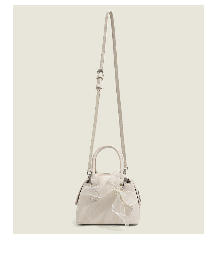 Small structured Boston bag in cream with glossy crinkled finish, sheer bow accent, silver-tone hardware, dual top handles