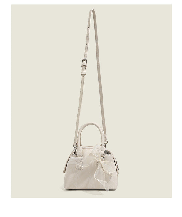 Small structured Boston bag in cream with glossy crinkled finish, sheer bow accent, silver-tone hardware, dual top handles