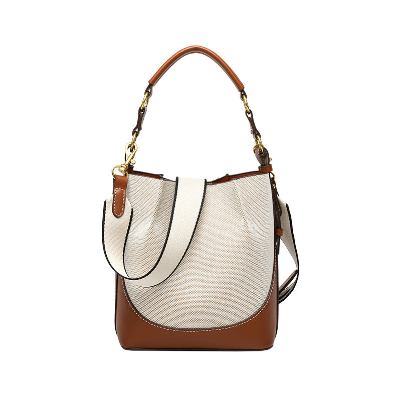 Cream canvas and tan leather-look bucket bag with arched top handle, wide detachable shoulder strap, and gold-tone hardware