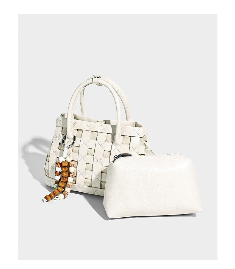 Small structured woven satchel tote with rounded top handles, silver-tone ring hardware, and bead tassel charm, detail view