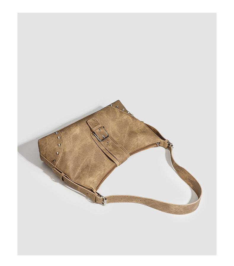 Slouchy trapezoid hobo shoulder bag with distressed textured finish, silver rivet corner accents, centre buckle strap, and