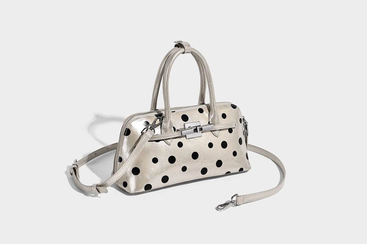 Glossy structured polka-dot satchel bag with dual top handles, silver turn-lock hardware, and detachable shoulder strap