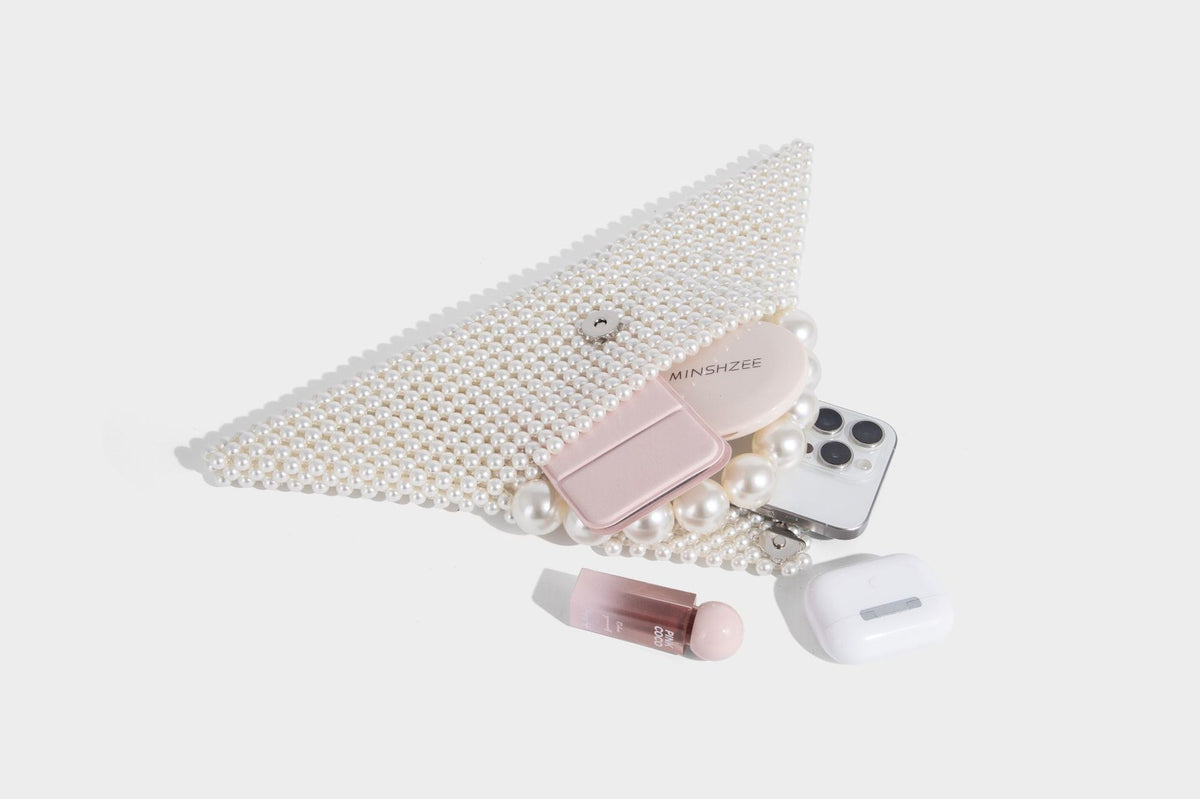 Small structured triangle clutch bag covered in glossy pearl beads with an arched pearl top handle and silver snap closure