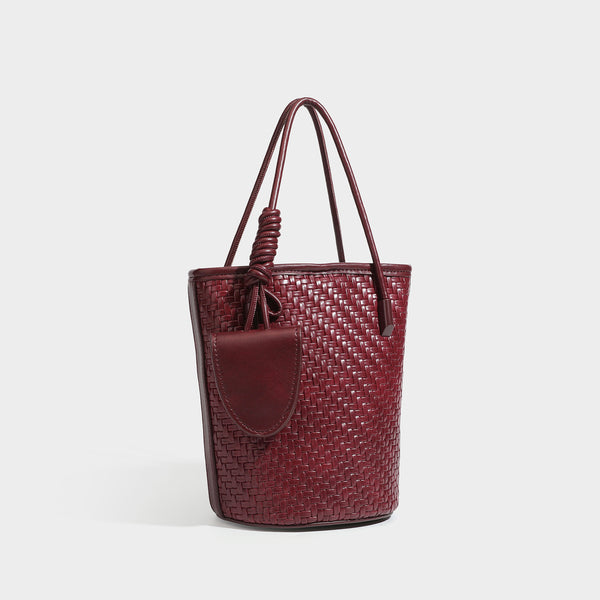 Structured woven-texture leather-look bucket bag in brown with knotted top handles, small front flap pouch, and adjustable