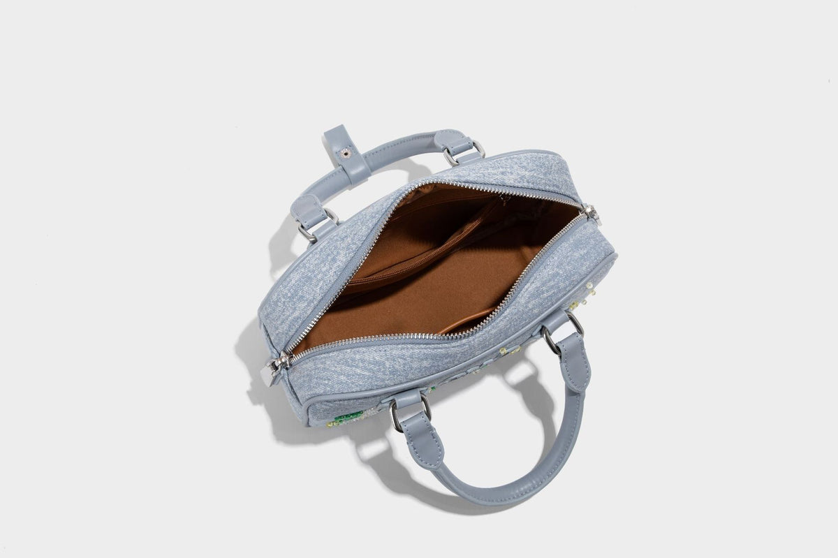 Small light blue denim-look barrel bag with white floral bead embroidery, dual top handles, and detachable shoulder strap