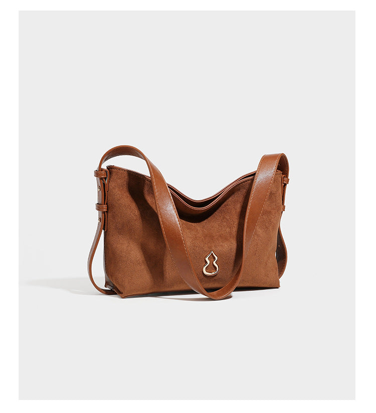 Slouchy suede-finish brown shoulder bag with long single strap and small gold-tone logo emblem on front, detail view 10