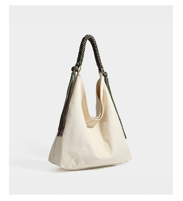 Soft slouchy cream canvas shoulder tote with braided brown and green cord handle, gold-tone ring hardware, and tassel trim