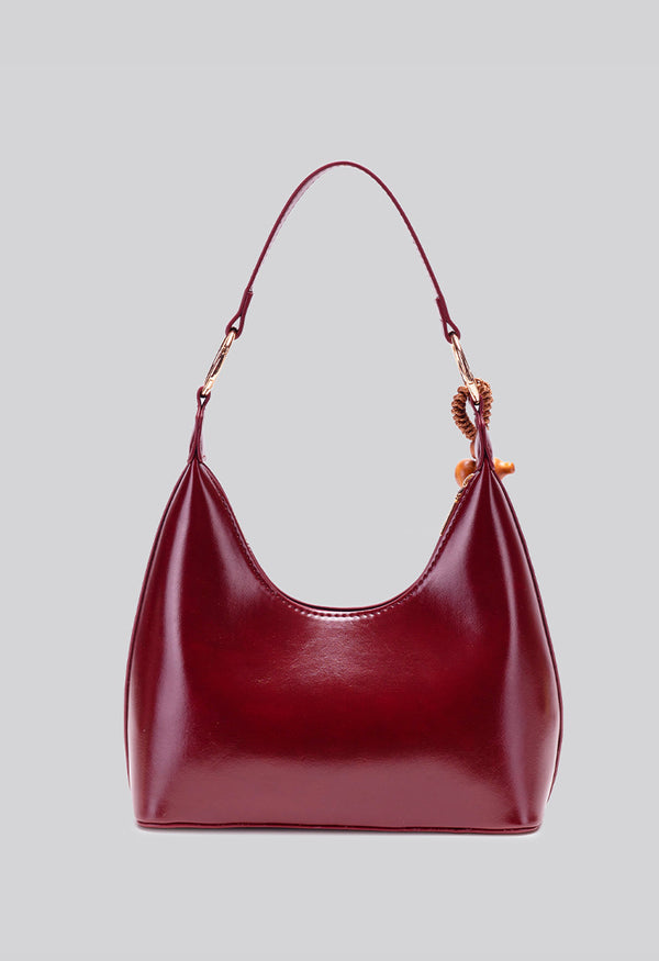 Glossy crescent hobo shoulder bag in deep burgundy with beaded wood tassel charm and gold-tone ring hardware, detail view 10