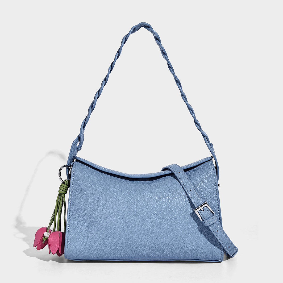 Small structured pebbled-finish shoulder bag with braided top handle, detachable crossbody strap, floral tassel charm, and