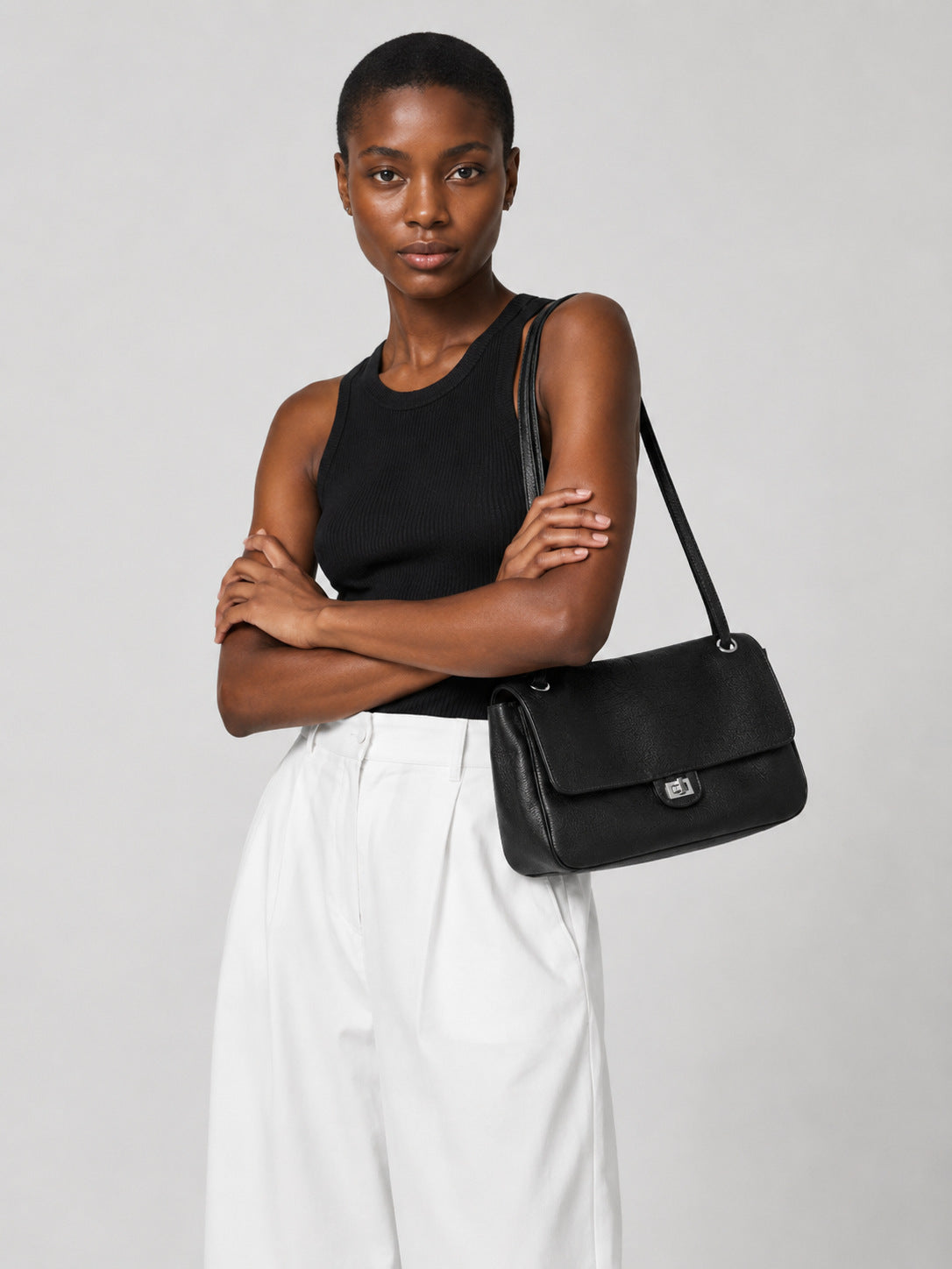 Structured black flap shoulder bag with pebbled texture, silver-tone turn-lock closure, and adjustable single shoulder strap