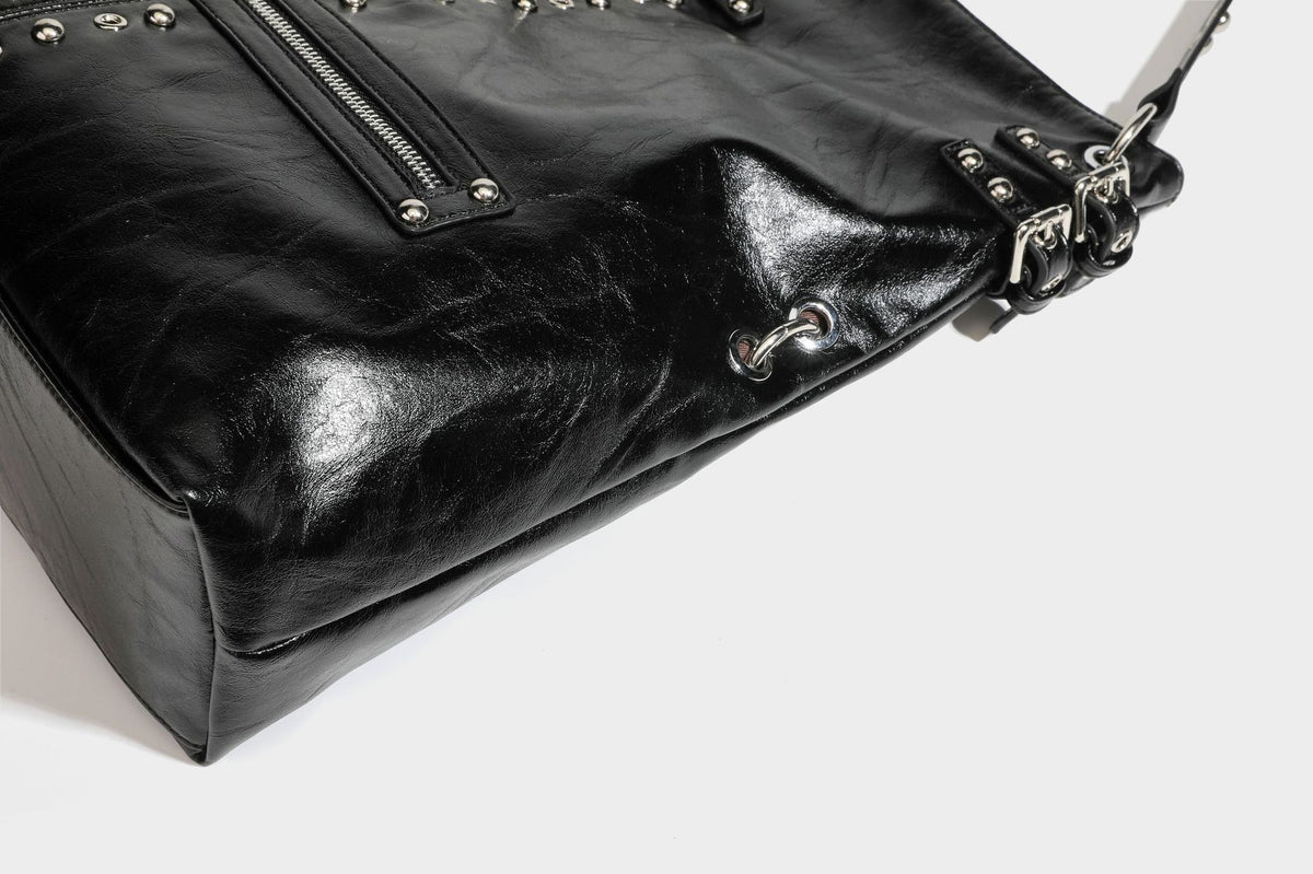 Black glossy leather-look slouchy shoulder bag with silver stud and eyelet hardware, top zip closure, front zip pocket, and