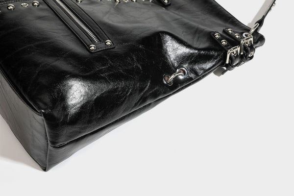 Black glossy leather-look slouchy shoulder bag with silver stud and eyelet hardware, top zip closure, front zip pocket, and