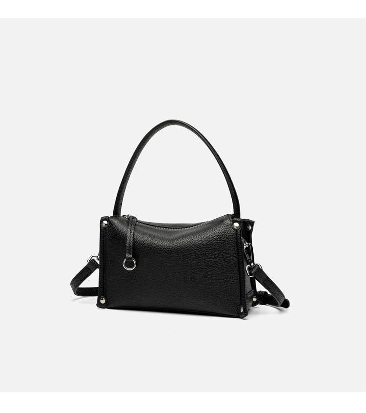 Small structured pebbled-finish convertible bag with silver corner studs, zip top, and detachable shoulder strap, detail view