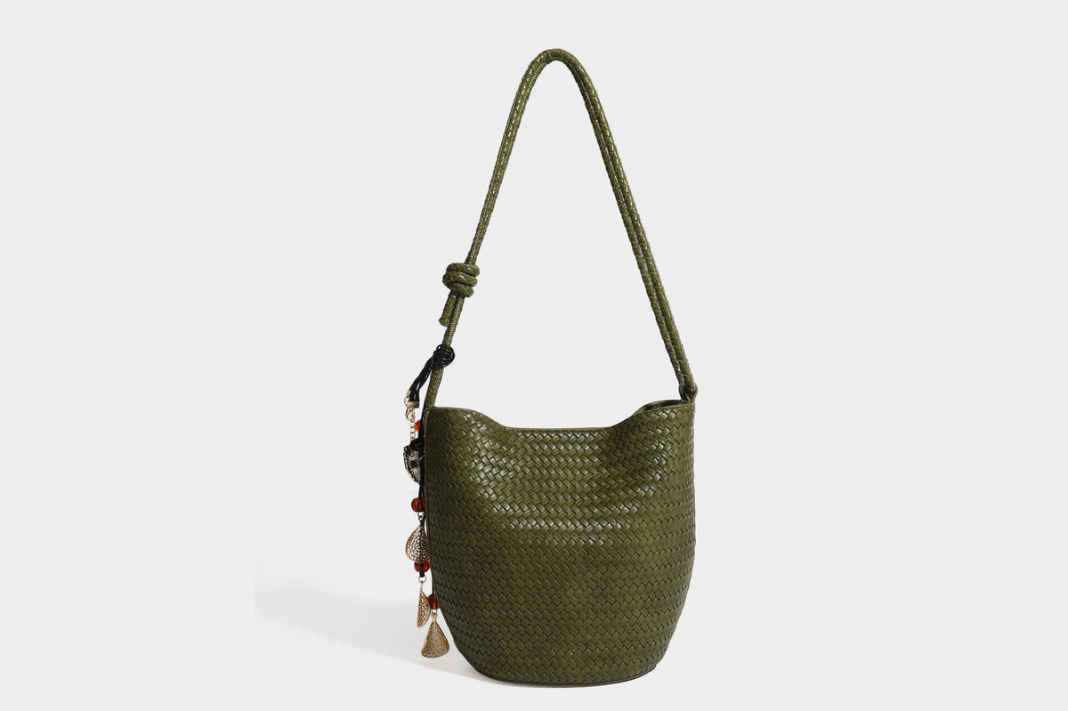 Olive green woven leather-look bucket bag with braided crossbody strap, knotted adjustment, and gold-tone tassel charm with