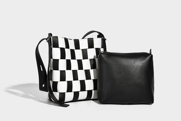 Hand-woven black-and-white checkerboard bucket bag with smooth black trim, silver-tone ring hardware, and adjustable