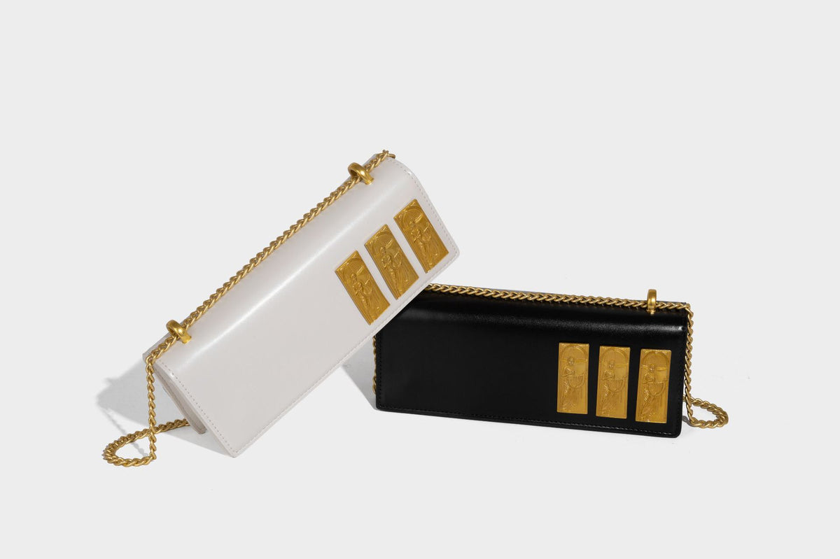 Structured rectangular crossbody bag with glossy finish, three vertical gold-tone embossed plaques, and gold chain strap
